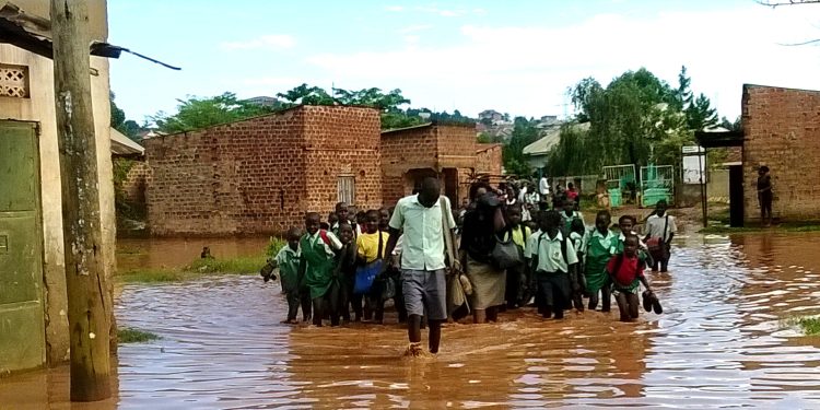 In the low-lying suburb of Bwaise, lines of school children, uniforms drenched and shoes in hand, wading waist-deep through dirty, fast-moving floodwaters on their way home from school. Courtesy photo.