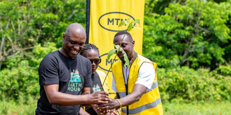 Ibrahim Senyonga, GM EBU at MTN Uganda, plants a tree as Bunyoro Kingdom Prime Minister Andrew Byakutaka, dressed in a suit, and partner’s staff look on during the Earth Hour commemoration in Kikuube District