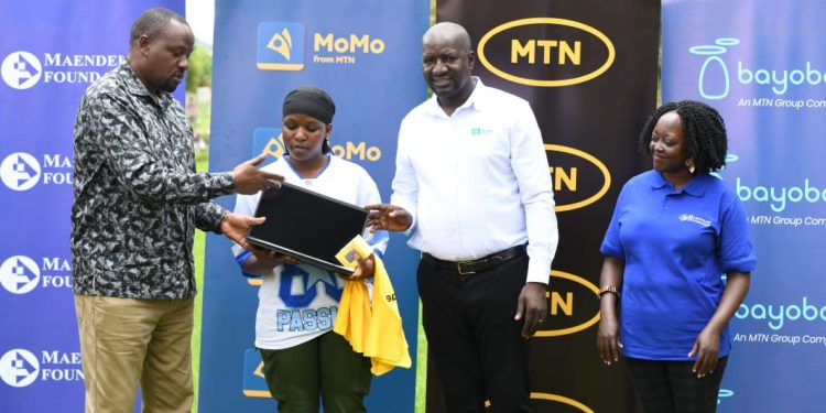 Bushenyi RDC Emmy Ngabirano hands over a new laptop to Kanyonyore Vocational School student, Daphine Abaasa one of the top performers in the digital literacy training programme, as MTN Commercial Head Andrew Tusubira looks.