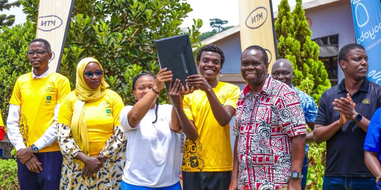 Godwin Kagibwami, in MTN T-shirt, receives a laptop courtesy of MTN Foundation as chief guest Micah Rwothumio congratulates graduands.