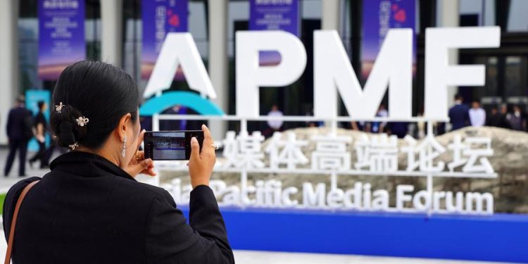 A guest takes photos of the logo of the Asia-Pacific Media Forum outside the venue of the forum in Shenzhen, south China's Guangdong Province